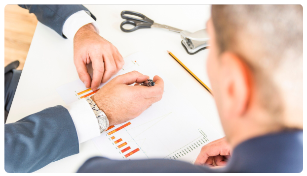 Hands reviewing a bar chart printout with a pen and scissors on a desk